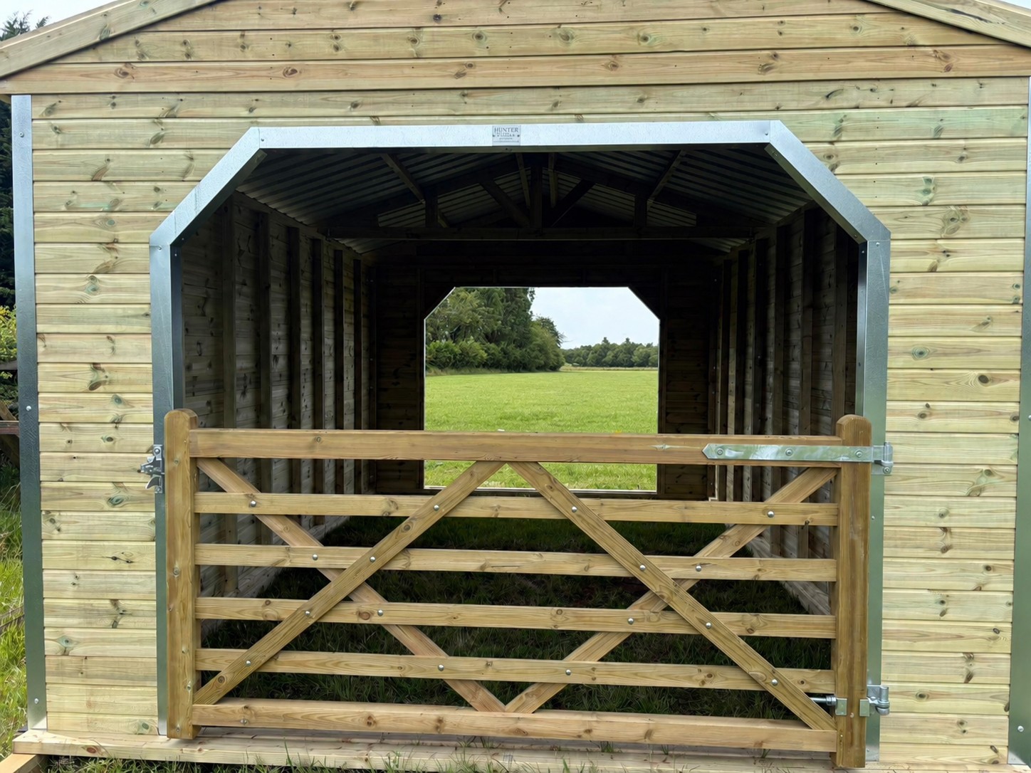Large 12 x 18 wooden walk through livestock and horse shelter with secure timber gates, durable galvanised framing, and countryside field backdrop.