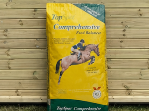 Topspec Comprehensive feed balancer 20kg leaning against a timber stable building